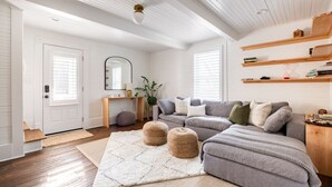 Un salon avec un canapé gris, des étagères en bois et une porte blanche.
