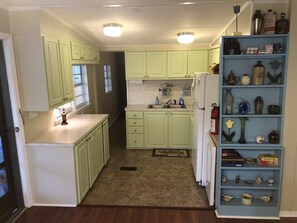A kitchen with light green cabinets, a white refrigerator, and a blue shelving unit with various items. - Private Lake House with Dock & Boat Ramp (Saluda)
