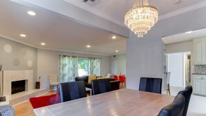 Un coin repas avec une table en bois et six chaises, un lustre et une cheminée.