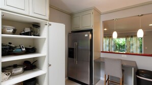 Une cuisine compacte avec des meubles blancs, un réfrigérateur en acier inoxydable et un petit coin bar équipé d’un tabouret.