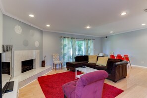 A modern living room with a fireplace, a sofa, a red rug, and a window with curtains.