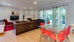 Un salon moderne avec une table à manger en verre, des chaises rouges, un canapé marron, un téléviseur à écran plat et une cheminée.