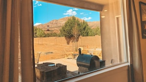 A window view of a backyard with a barbecue grill, a wooden table, and a chair.