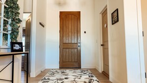 A hallway with a wooden door, a hanging plant, a framed picture on a shelf, and a patterned rug.