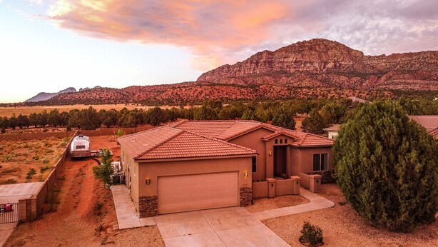A single-story house with a garage, surrounded by a fenced yard, set against a mountainous backdrop.