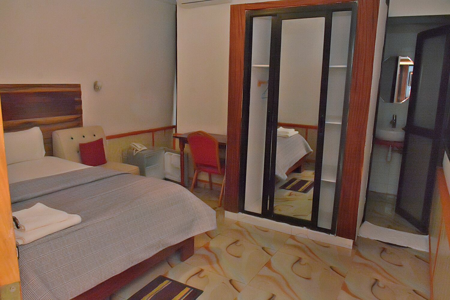 Ein Hotelzimmer mit Bett, Schreibtisch, Stuhl, Kleiderschrank und einem durch eine Glastür sichtbaren Badezimmer.