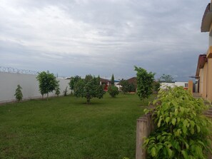 A grassy yard with several trees and a white wall with barbed wire. - Florence Hotel Firenze Yamoussoukro (Yamoussoukro)