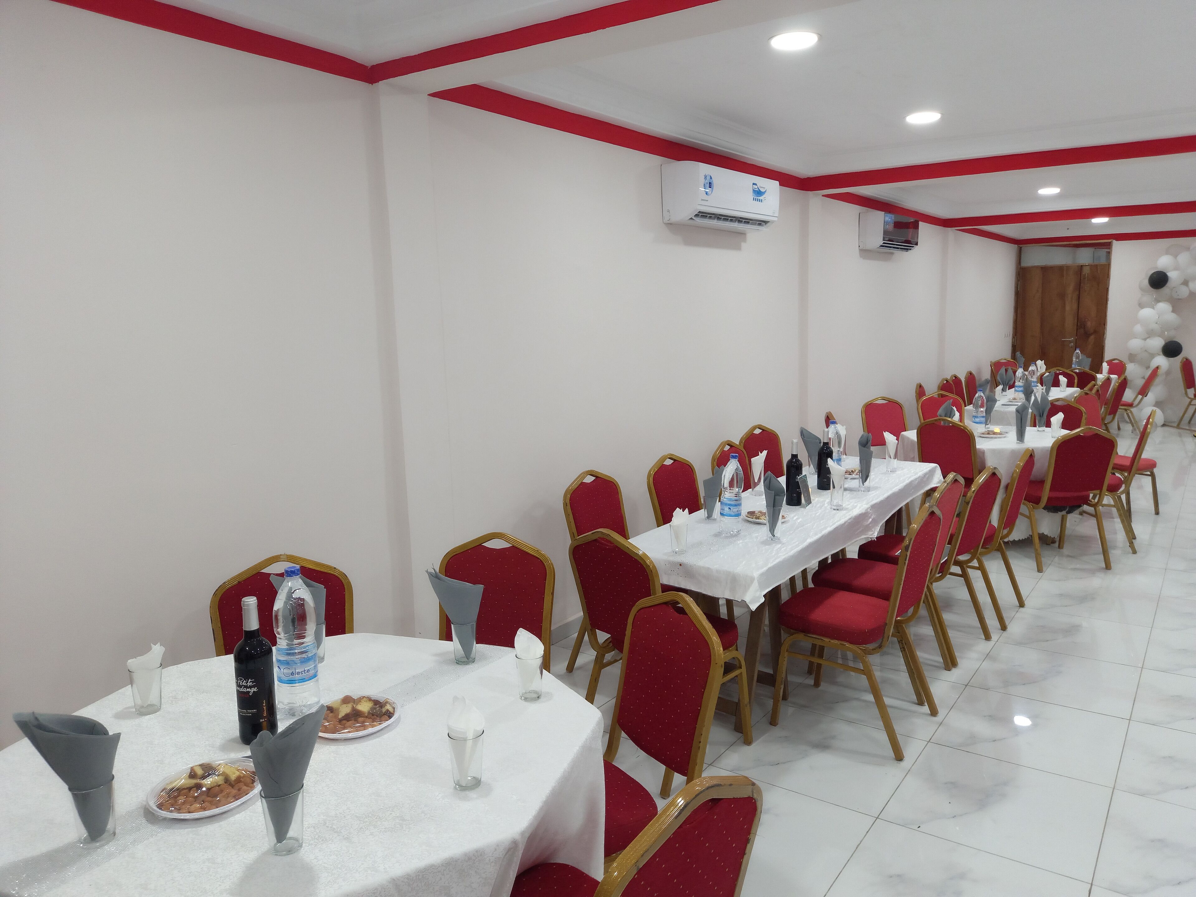 Une salle de conférence avec des tables rondes, des chaises rouges et des nappes blanches.