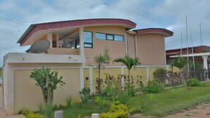 A two-story building with a curved roof, satellite dish, and a fenced garden with various plants. - Florence Hotel Firenze Yamoussoukro (Yamoussoukro)