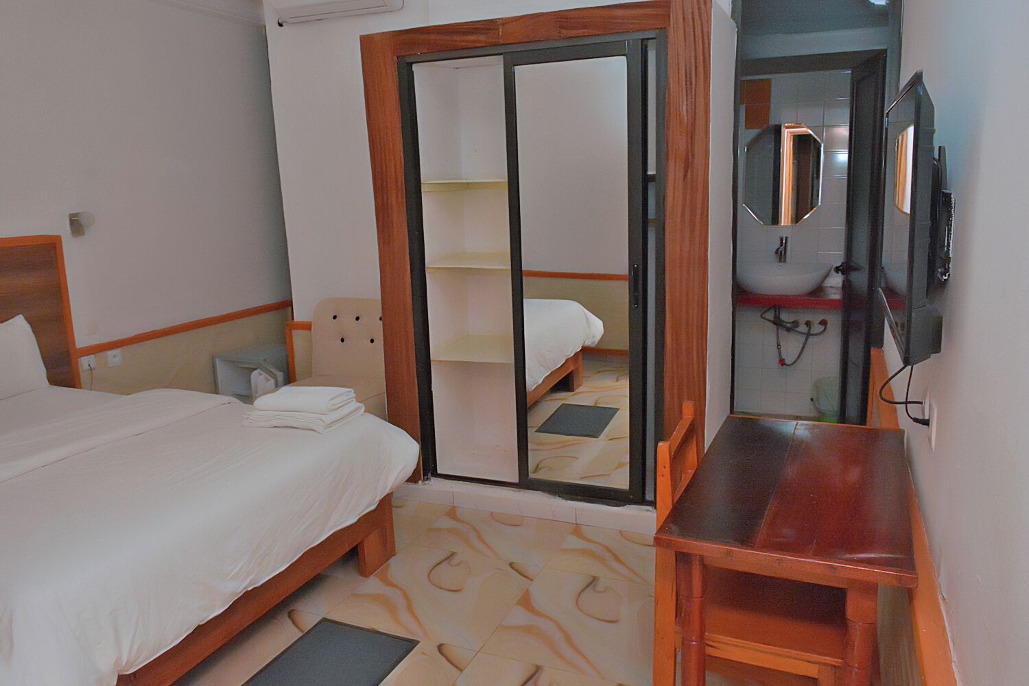 A hotel room with a bed, a wooden nightstand, a mirror, and a sliding door leading to a bathroom.