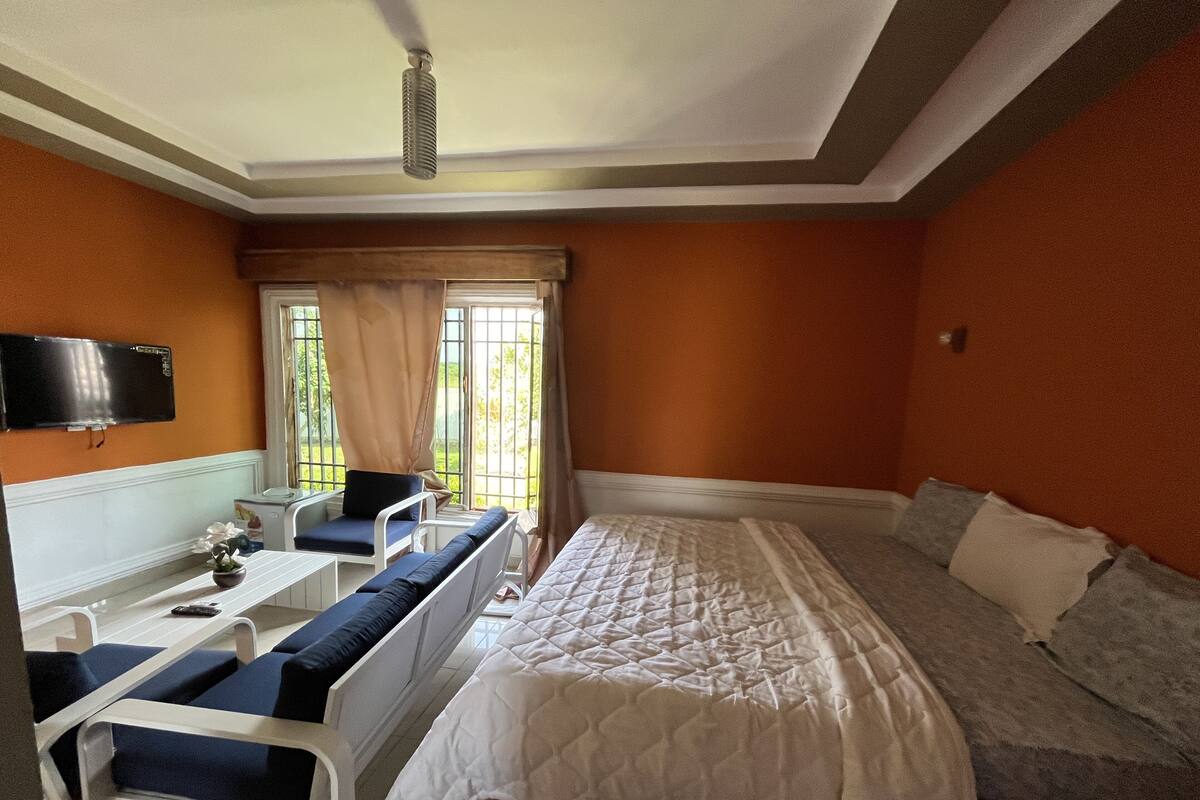 A bedroom with a bed, a desk, and a chair. There is a television on the wall and a window with curtains.