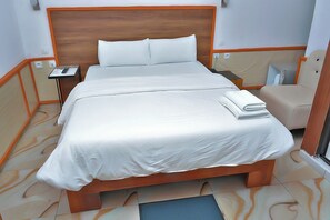 A neatly made bed with white linens, a wooden headboard, and a bedside table with a remote control. - Florence Hotel Firenze Yamoussoukro (Yamoussoukro)