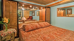 Ein Schlafzimmer mit Holzbalkendecke, einem großen Bett mit gemustertem Überwurf, einem Nachttisch mit Blumenvase und einem Spiegel, der den Raum widerspiegelt.