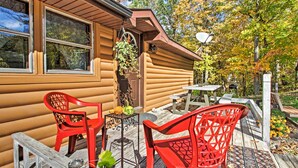 Eine Blockhütte mit einer Terrasse, auf der rote Stühle und ein kleiner Tisch stehen.
