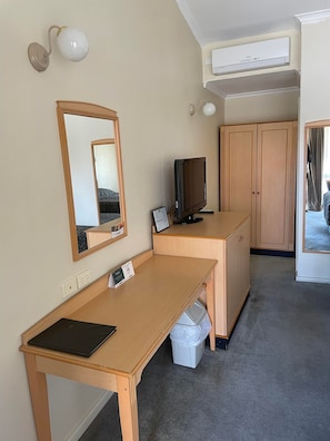 Quarto de hotel com escrivaninha de madeira, televisão, espelho e guarda-roupa.