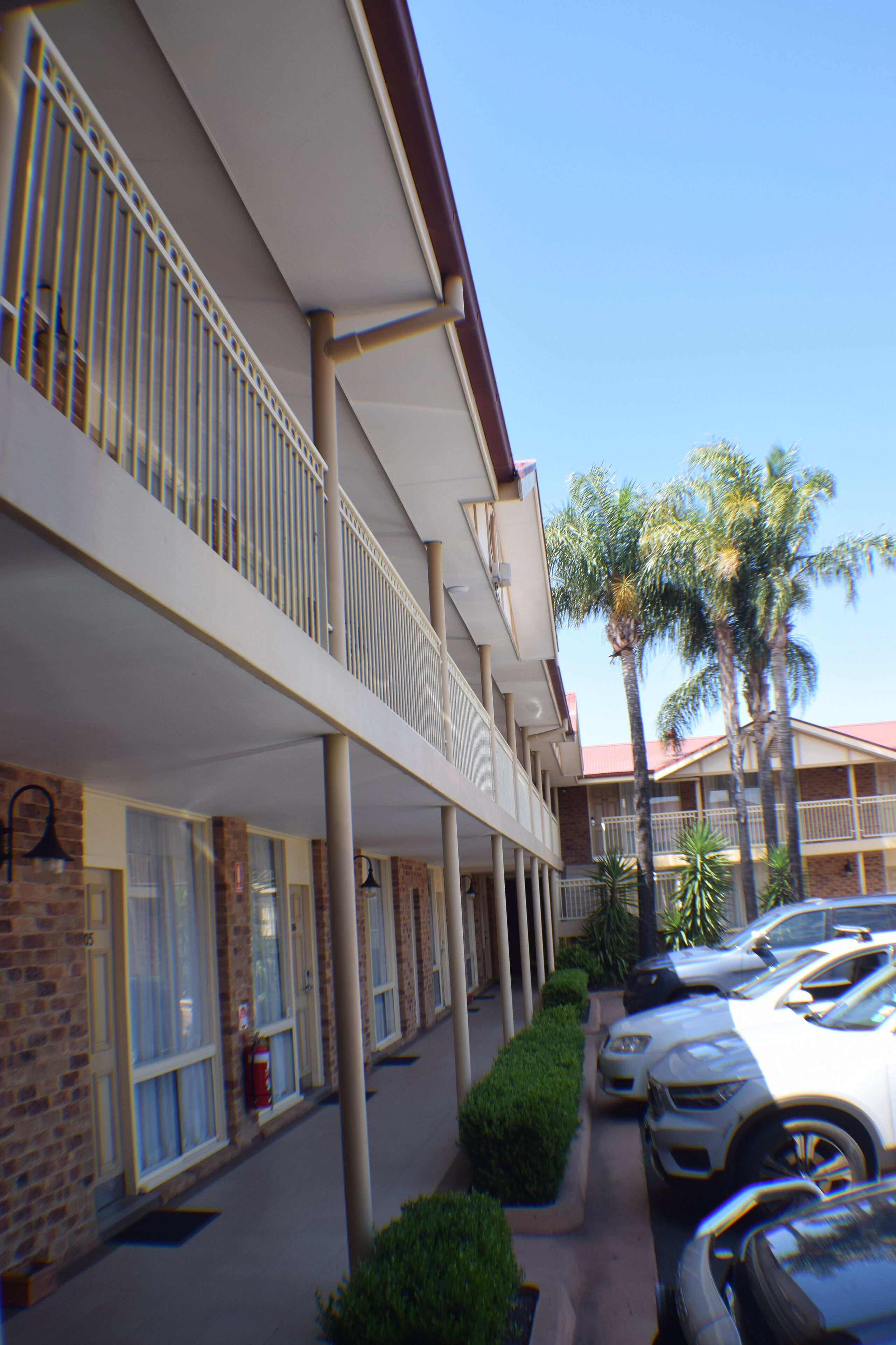 A hotel with a covered outdoor area, multiple floors, and parked cars.