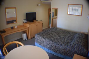 A hotel room with a bed, a desk with a computer, a television, and a mirror.