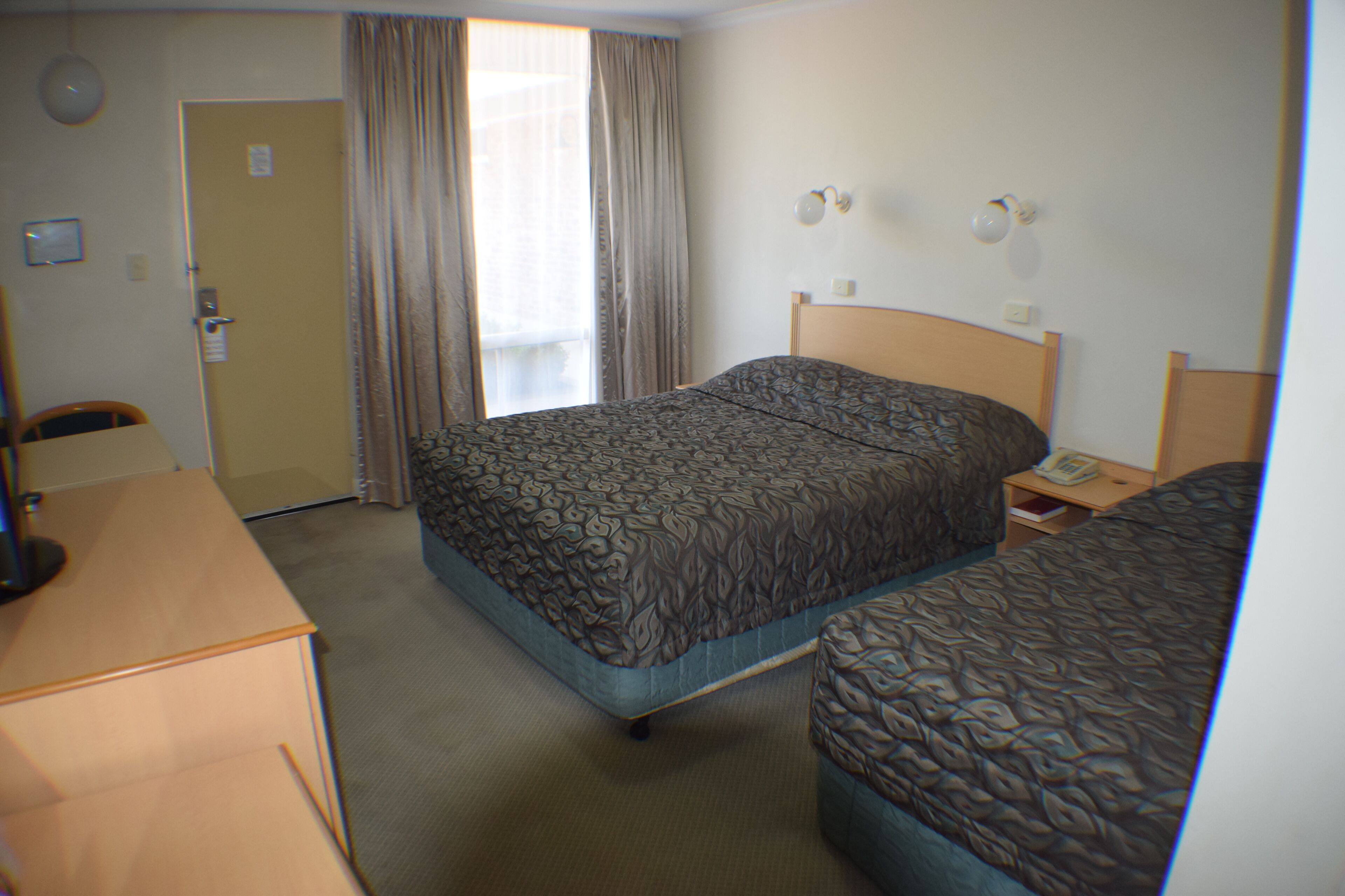 Une chambre d’hôtel avec deux lits, un bureau, une chaise et une fenêtre avec des rideaux.