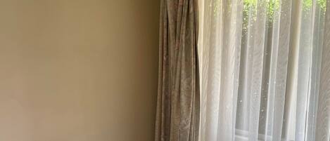A room with a round table and two chairs, a window with sheer curtains, and a carpeted floor.