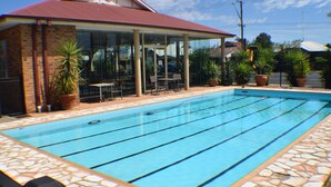 Una piscina con baldosas de piedra, una zona de estar techada con mesas y sillas, y plantas en macetas.