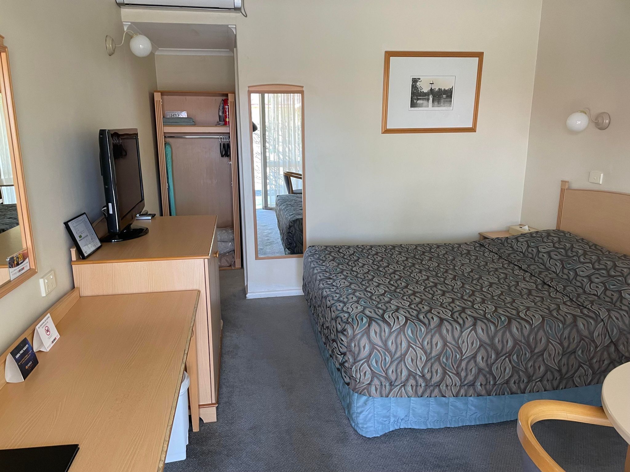 Una habitación de hotel con cama, escritorio, televisión y armario.