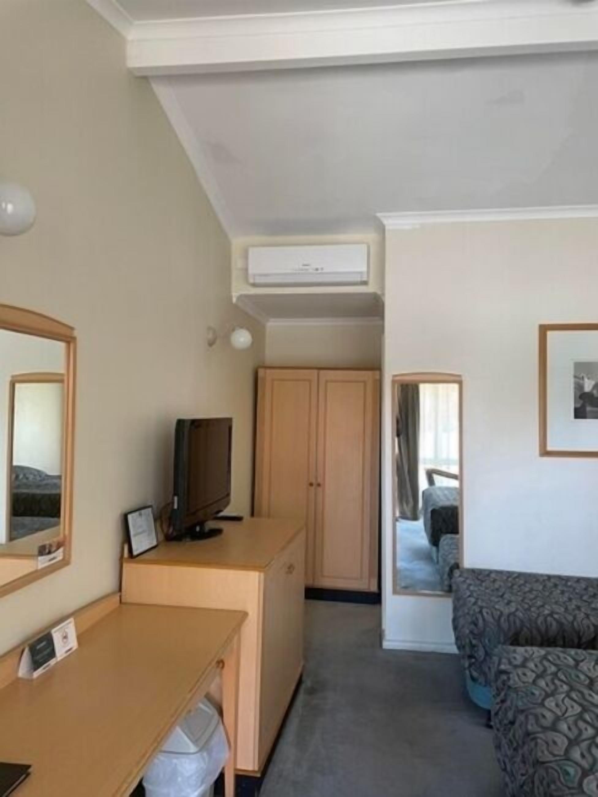A hotel room with a desk, a television, a wardrobe, and a bed.
