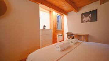 A bedroom with a wooden ceiling, a bed with white linens, a wooden desk, and a framed picture on the wall.