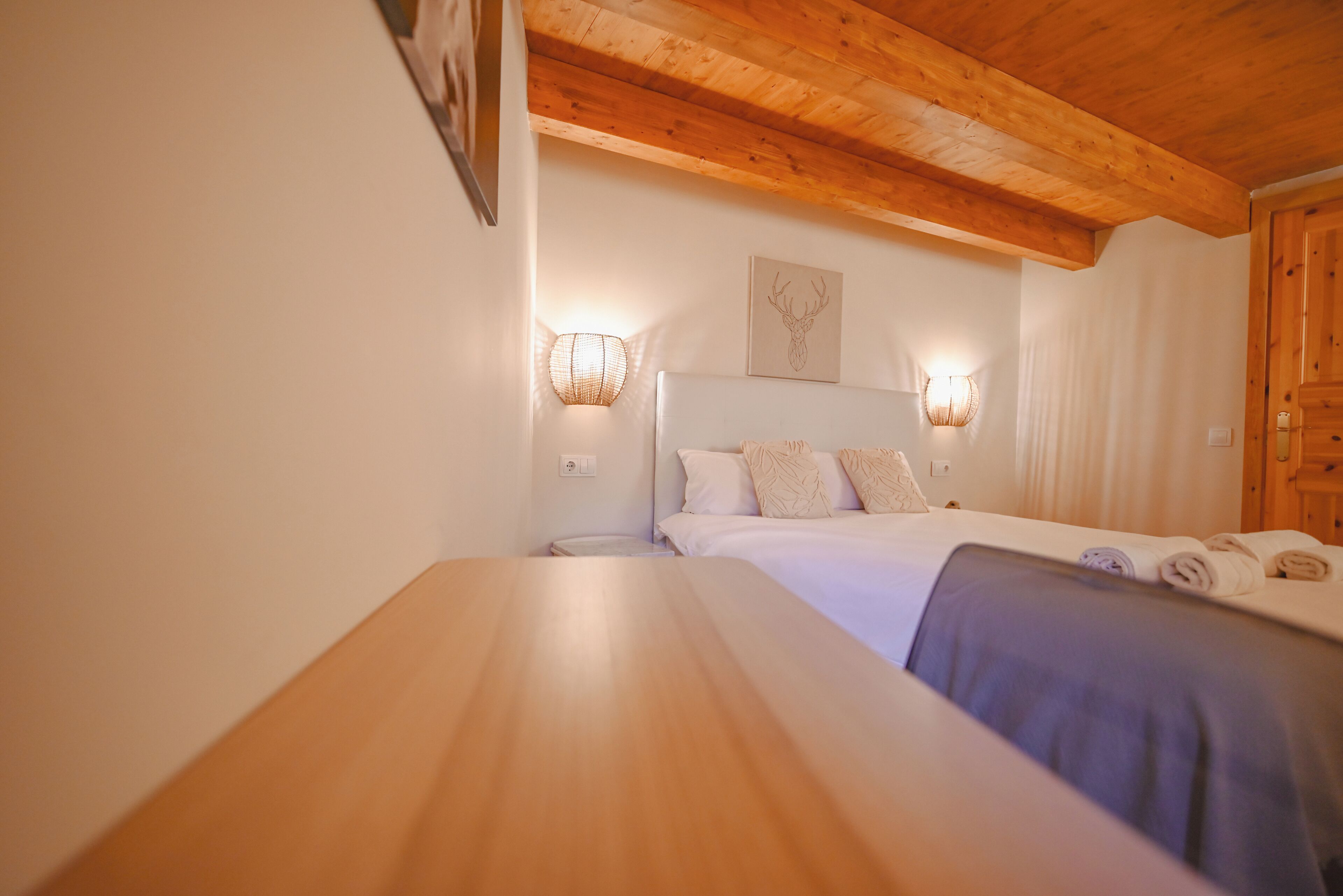 Ein Schlafzimmer mit Holzbalkendecke, zwei Nachttischen, einem Bett mit weißer Bettwäsche und Wandleuchten.