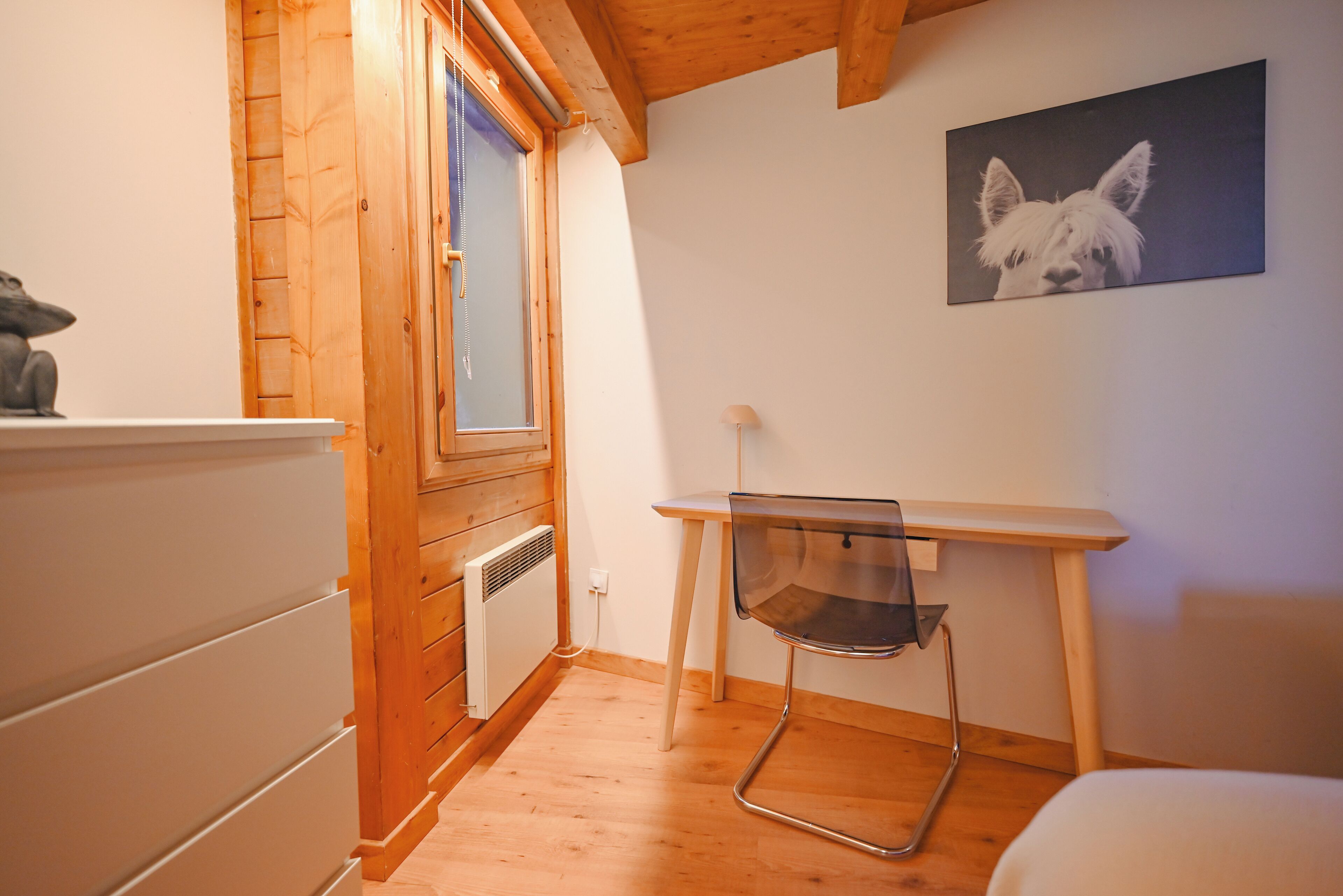 A small room with wooden walls and a window, a chair, and a picture on the wall.