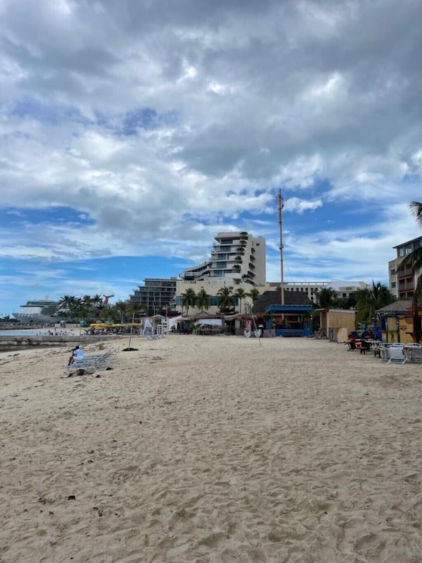 A beach with a hotel in the background, featuring multiple floors and balconies.