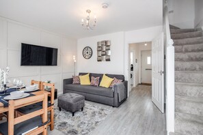 A modern living room with a grey sofa, wooden dining table, and a flat-screen TV mounted on the wall. - 2 bedroom with 2 bathrooms stylish house in Dartford Kent (Dartford)