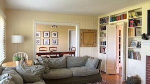 Ein Wohnzimmer mit Ecksofa, einem Esstisch mit Stühlen, einem Bücherregal und einem gemusterten Teppich.