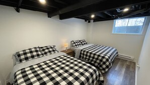 Una habitación con dos camas, cada una con una colcha a cuadros, una mesita de noche con una lámpara y una ventana con persianas.