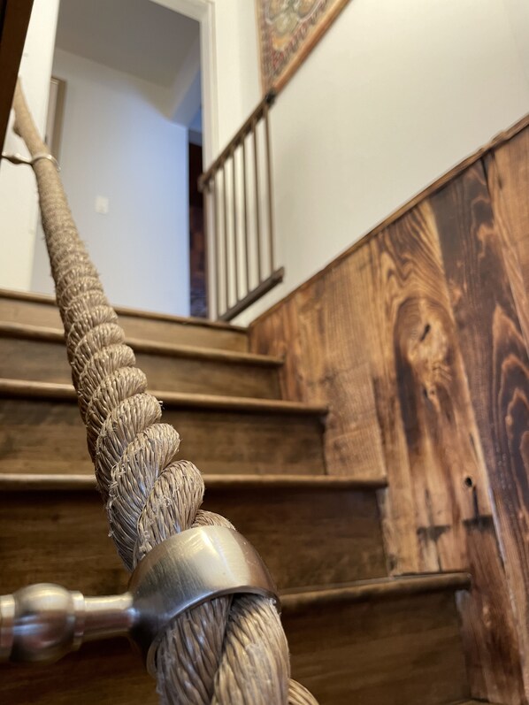 A close-up of a wooden staircase with a metal railing and a textured wall.
