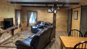 Un accogliente interno di una baita con un divano in pelle, un tavolo da pranzo in legno e un televisore su un mobile in legno.
