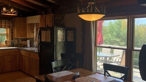 Una cucina rustica con travi in legno, un tavolo da pranzo con sedie, un frigorifero e un'ampia finestra con vista su un patio.