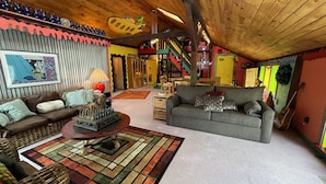 A cozy living room with a wooden ceiling, a chessboard centerpiece, and a colorful rug.