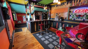 A colorful bar area with a wooden bar counter, stools, and a neon 'OPEN' sign.