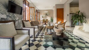 Uma sala de estar com piso xadrez, uma televisão de tela plana na parede e uma planta grande.