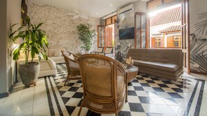 Uma sala de estar com piso xadrez, um sofá, uma mesa de centro e cadeiras de vime.