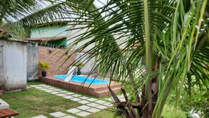 A backyard with a swimming pool, a palm tree, and a wooden bench.