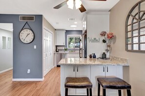 Una cocina moderna con armarios blancos, encimera de granito y un reloj en la pared.