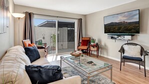 Una sala de estar moderna con una mesa de centro de vidrio, un sofá, un sillón y un televisor montado en la pared.