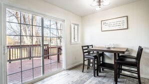 A dining area with a table and chairs, a window with a view of a deck, and a wall-mounted sign. - Big Sky Hotelier - Outstanding Sauna House (Billings)