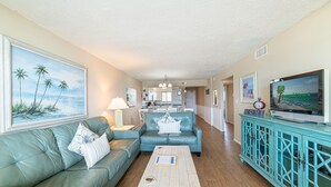 A living room with a teal sofa, a coffee table, and a television on a cabinet. - Beach Memories Made Here-The Memory Maker Regency Towers 407-Beachfront-2Bd/2Ba-Sleeps 8 (Panama City Beach)