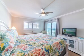 Un dormitorio con cama, ventilador de techo, televisor y vista al océano.
