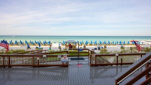 A wooden boardwalk leading to a beach with blue umbrellas and American flags. - Beach Memories Made Here-The Memory Maker Regency Towers 407-Beachfront-2Bd/2Ba-Sleeps 8 (Panama City Beach)