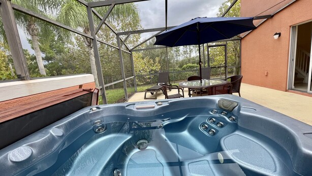 Un jacuzzi con recinto de vidrio, mobiliario exterior y un patio con vistas a árboles.
