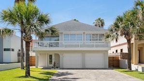 A two-story house with a balcony, a garage, and palm trees.