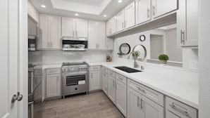 A modern kitchen with white cabinets, stainless steel appliances, and a black countertop sink.